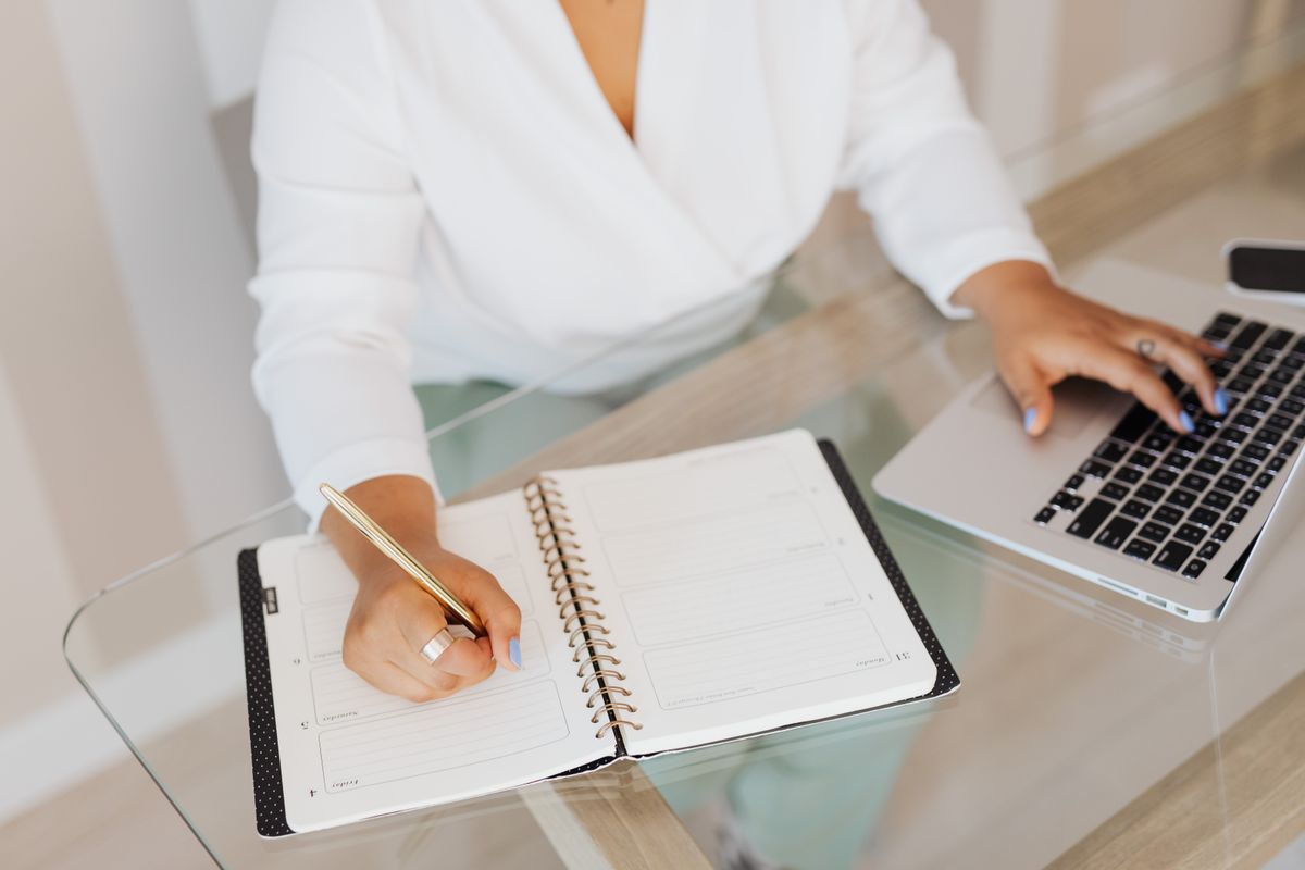 Personne écrivant sur carnet avec laptop